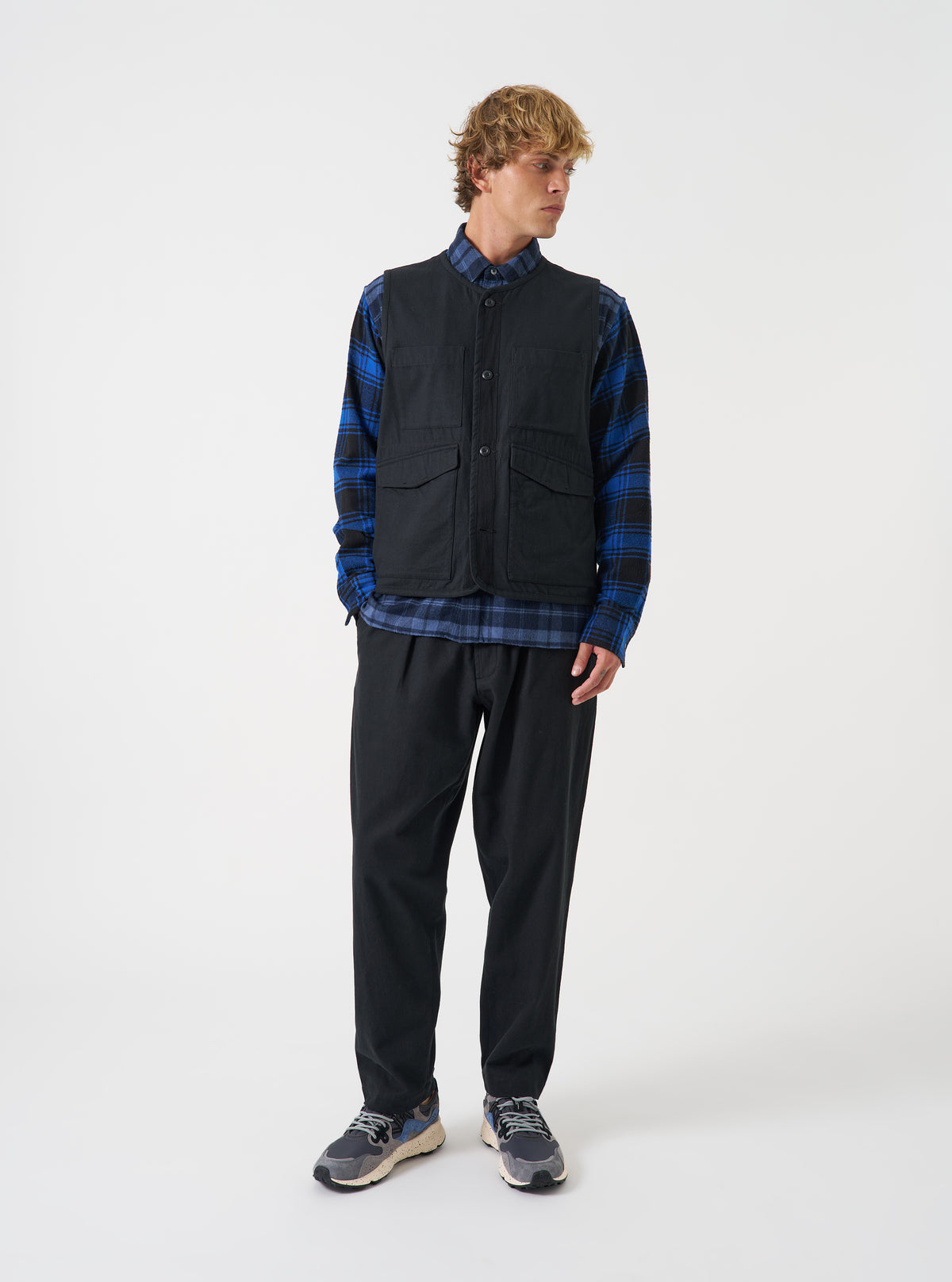 A model wearing the Universal Works Black Brushed Moleskin 4 Pocket Gilet, viewed from the front. The sleeveless black vest displays a round neck, central front button fastening, and four prominent front patch pockets against a plain background.