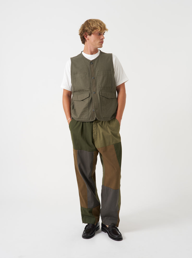 A model wearing the Universal Works Olive Brushed Moleskin 4 Pocket Gilet, captured from the front. The olive green vest features a round neckline, central button placket, two open chest pockets, and two lower flap pockets against a plain backdrop.