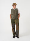 A model wearing the Universal Works Olive Brushed Moleskin 4 Pocket Gilet, captured from the front. The olive green vest features a round neckline, central button placket, two open chest pockets, and two lower flap pockets against a plain backdrop.