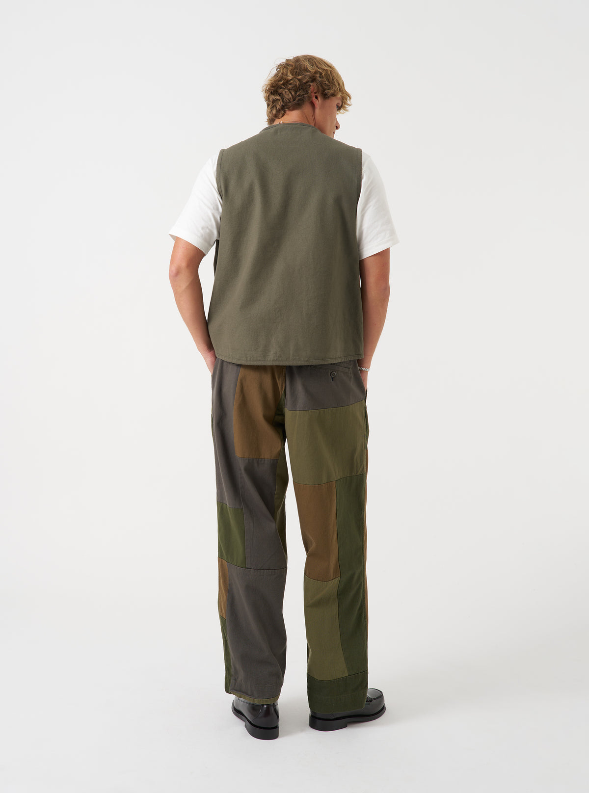 A back view of a model wearing the Universal Works Olive Brushed Moleskin 4 Pocket Gilet. The image shows the rear cut of the olive green brushed cotton waistcoat with a smooth back panel and relaxed silhouette set against a plain background.