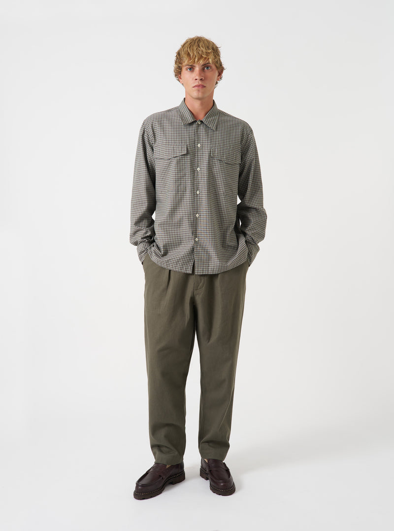 A model wearing the Universal Works Olive Brushed Moleskin Pleated Track Pant, shown from the front against a plain background. The olive green trousers feature front pleats, drawstring waist, side pockets, and a tapered leg fit.