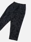 Flat lay of black wool mix track pants on a light grey seamless backdrop. The fabric features a tonal abstract jacquard pattern in varying depths of black. An elasticated waistband sits at the top with two small dark buttons visible on the front. The tapered legs are shown at full length with no cuffs.