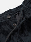 Close-up detail of the black wool mix pleated track pant's waistband and fly area. Two dark brown four-hole buttons fasten the placket. A woven drawcord threads through the ribbed elasticated waistband. The textured fabric shows a tonal check pattern. Shot against a plain light grey studio backdrop.