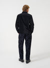 A back view of a model wearing the Universal Works Black Be Bop Wool Mix Pleated Track Pant against a plain background. The image showcases the dark printed wool-mix fabric, rear patch pockets, and loose fit tapering to the hem.