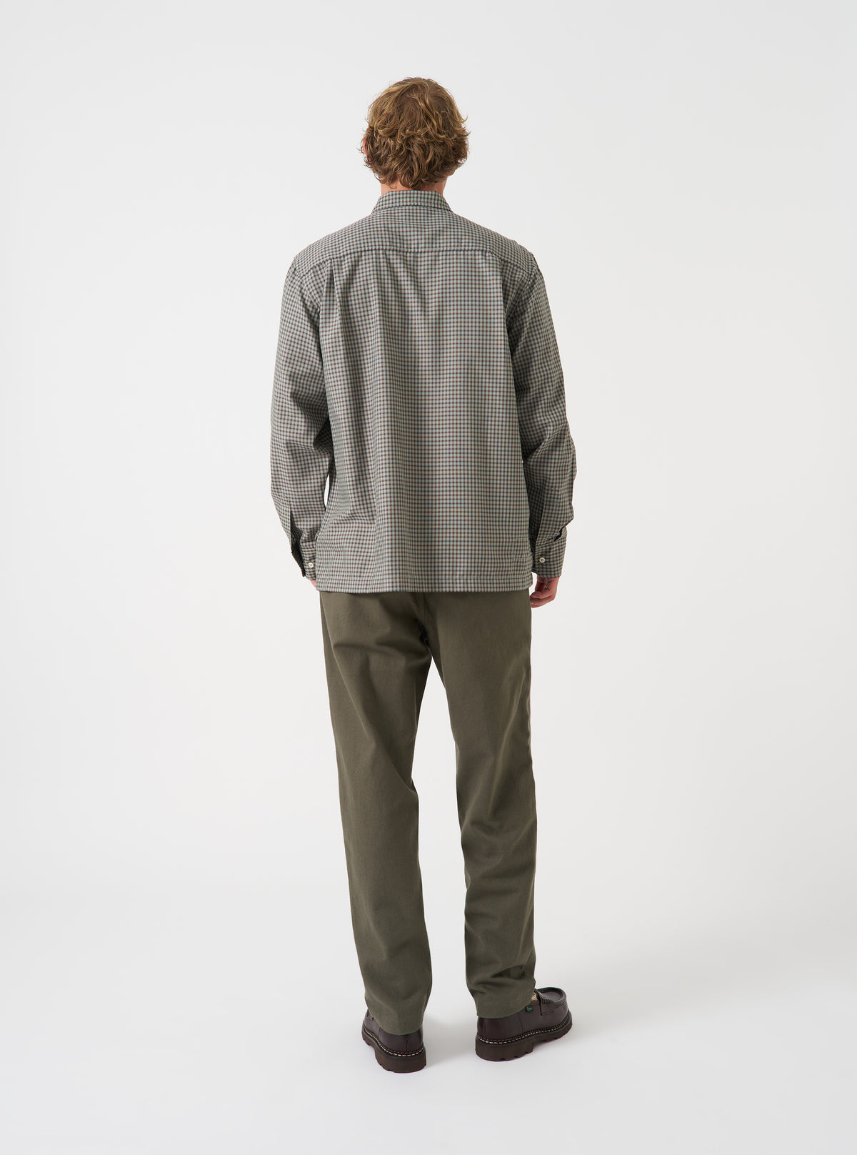 A back view of a model wearing the Universal Works Olive Brushed Moleskin Military Chino against a plain backdrop. The image displays the rear jetted pockets with button closures and the clean, tailored line of the olive trousers.