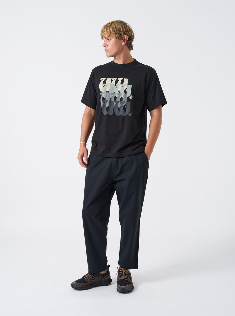 A model wearing the Universal Works Black Brushed Moleskin Hi Water Trouser, shown from the front against a plain background. The black cotton pants feature a cropped ankle length, elasticated drawstring waistband, and slim tapered fit.