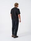 A rear view of a model wearing the Universal Works Black Brushed Moleskin Hi Water Trouser set against a plain backdrop. The image focuses on the cropped hemline above the ankle, dark brushed moleskin material, and back patch pockets.