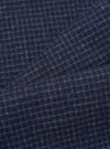 Close-up fabric shot of the navy check wool mix super chino, showing a fine grey windowpane check pattern on a deep navy ground. The brushed, slightly hairy texture of the wool mix fabric is clearly visible. A diagonal fold runs across the upper portion of the frame, revealing the fabric's drape.