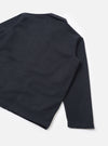 Flat lay of the navy wool mix bakers overshirt on a white studio surface, showing the back and one sleeve at an angle. The fabric features a tonal check pattern woven into the dark navy ground. The straight hem and unadorned cuff are visible, with a small collar visible at the top.