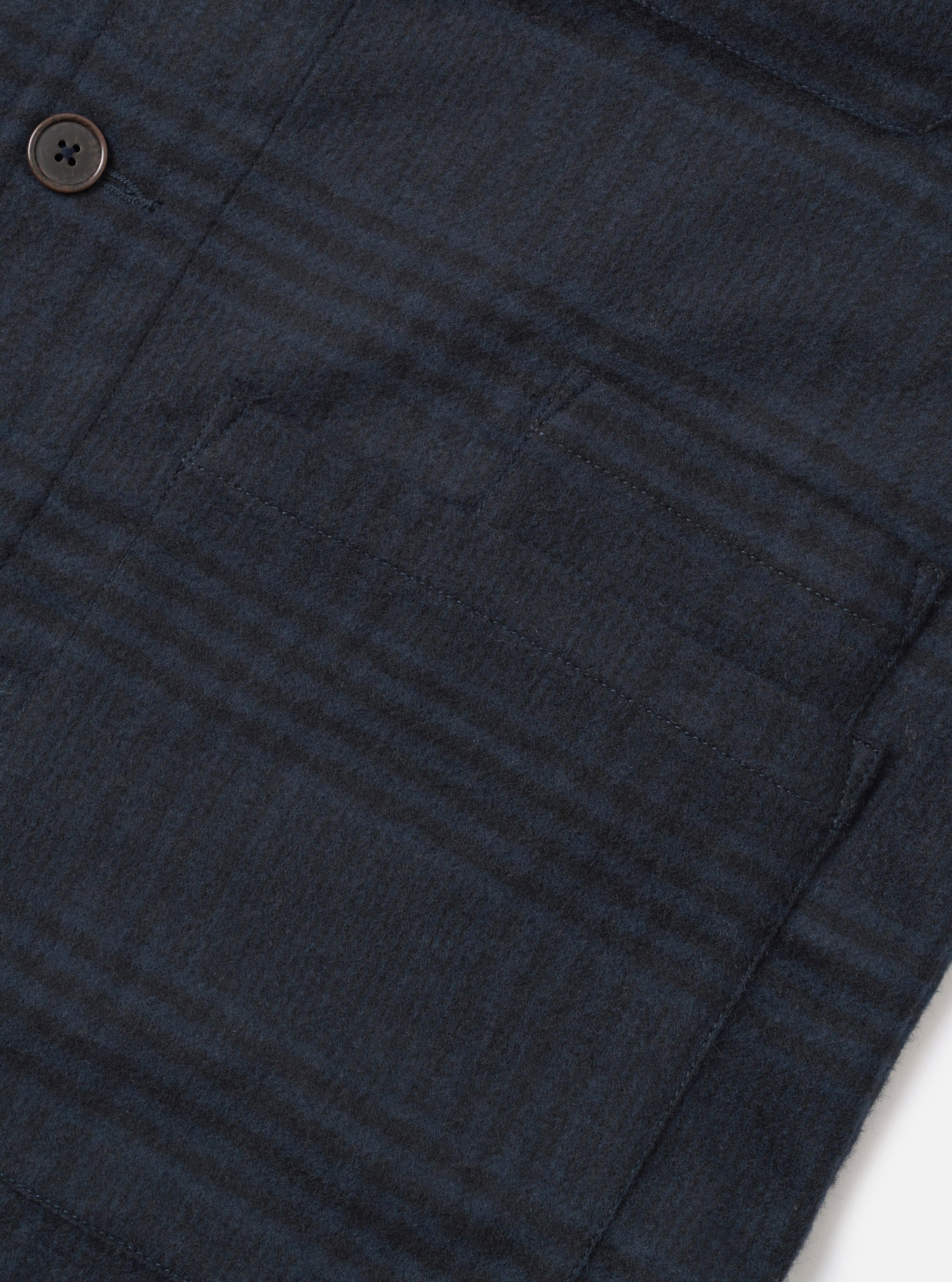 Close-up of the navy Bob wool mix bakers overshirt, showing a large patch pocket with topstitched edges and a dark horn-effect button above. The fabric has a textured wool mix weave with a tonal check pattern in navy and dark charcoal. Shot flat on a white surface.