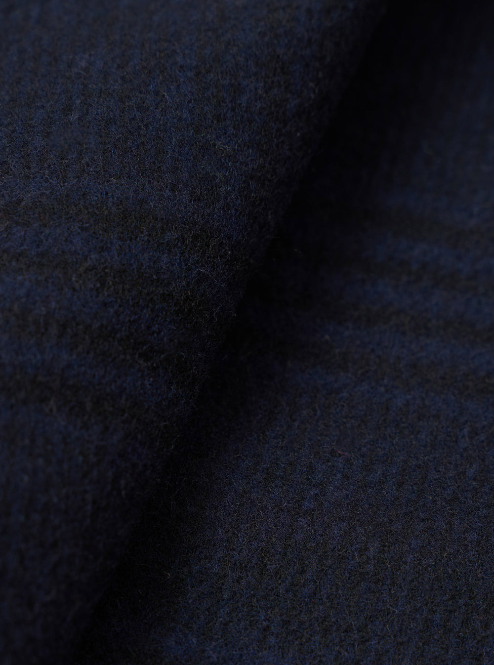Close-up of the navy wool mix fabric of a bakers overshirt, showing a dense, lightly brushed texture with subtle blue and dark grey tonal variation. The fabric has a soft, boiled-wool-style surface with fine surface fibres visible throughout. No background is visible.