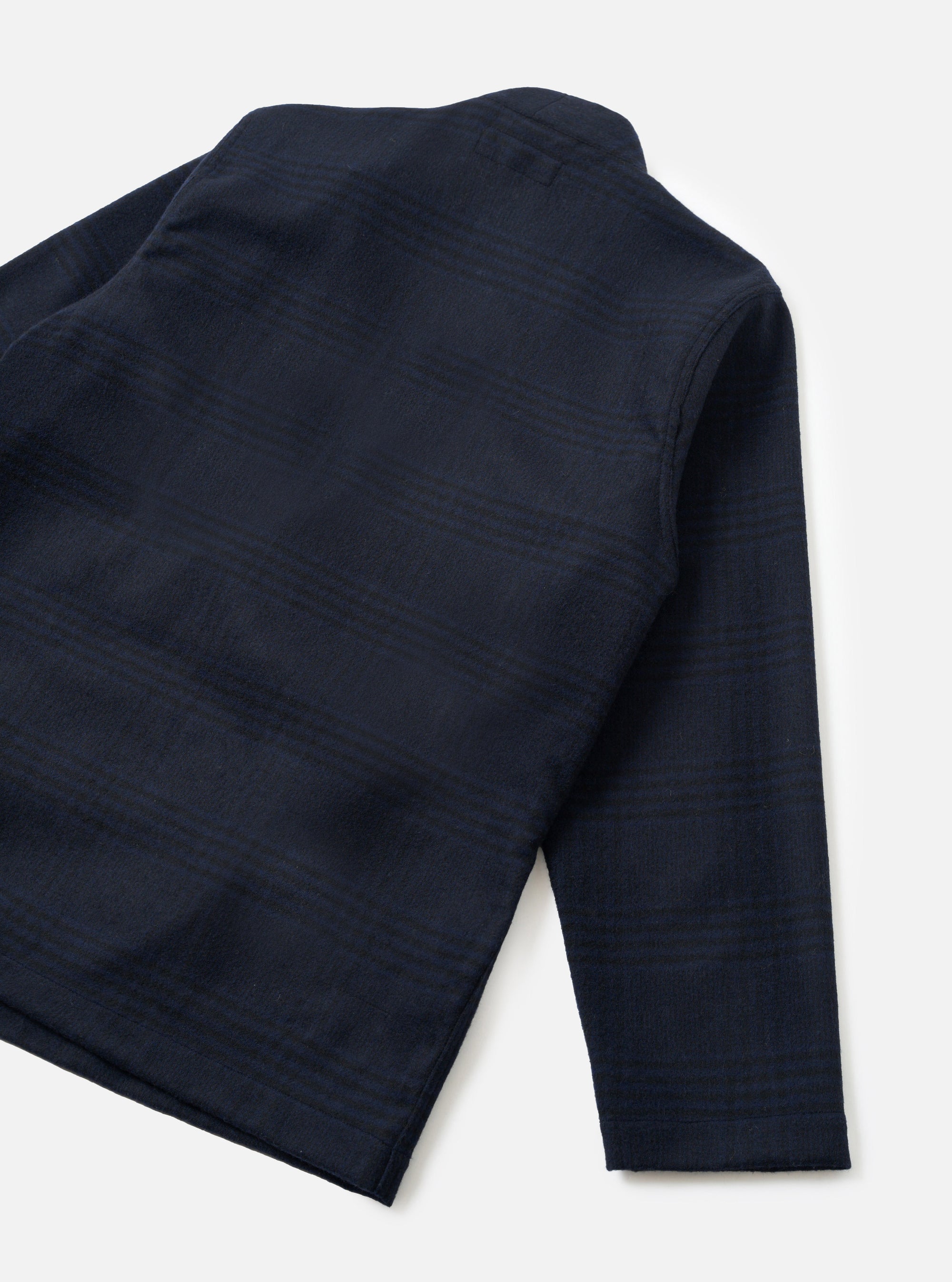 Back view of a navy wool mix Kyoto work jacket laid flat on a white studio surface. The fabric features a tonal check pattern in dark navy. Visible details include a stand collar, a single sleeve, and a clean straight hem. The check weave has a subtle texture throughout.