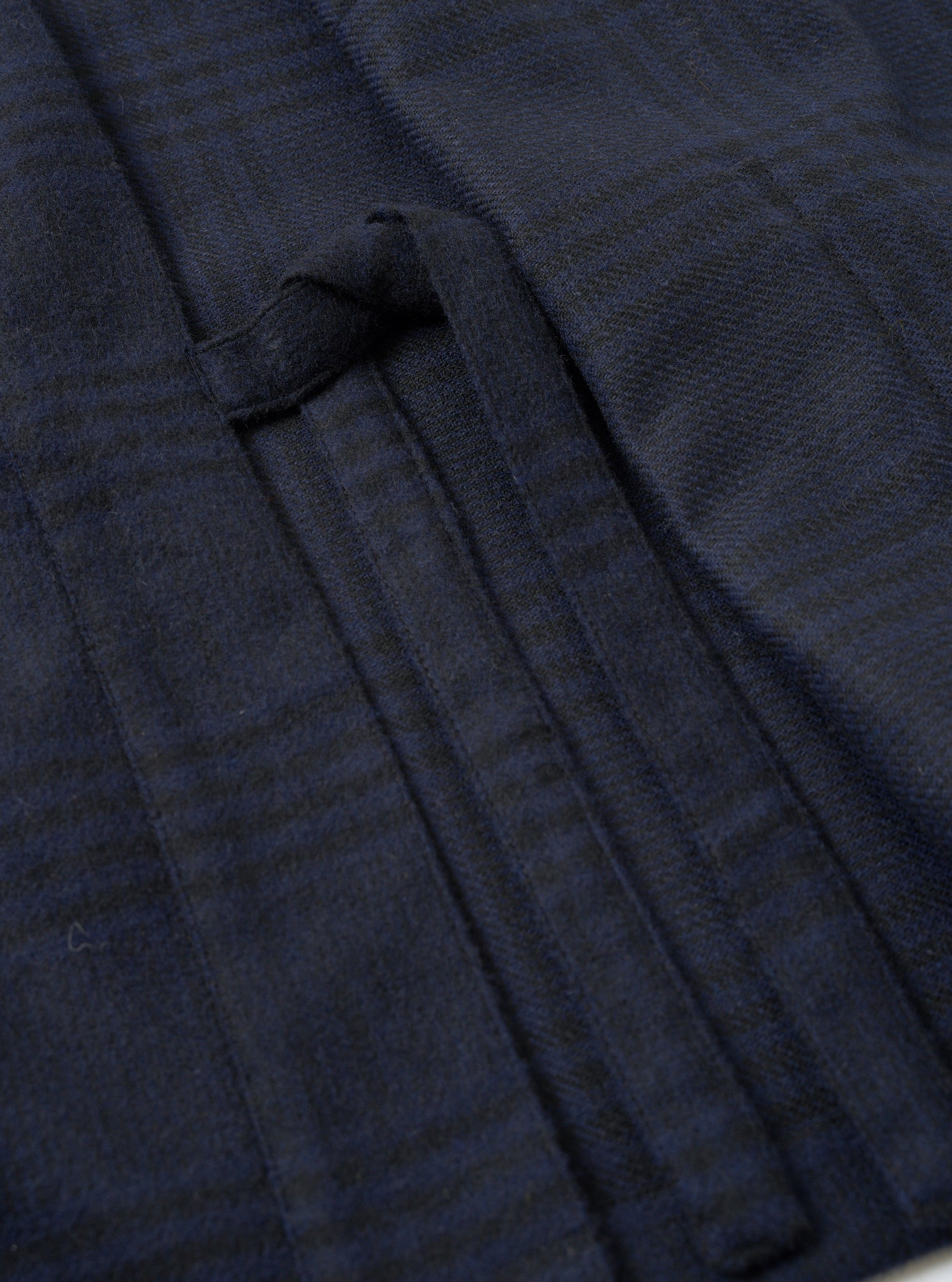 Close-up detail of the navy wool mix Kyoto Work Jacket showing a welt pocket with a fabric tab fastening. The tonal navy and dark green check pattern is visible across the brushed wool mix fabric. Shot flat, no model or mannequin present.