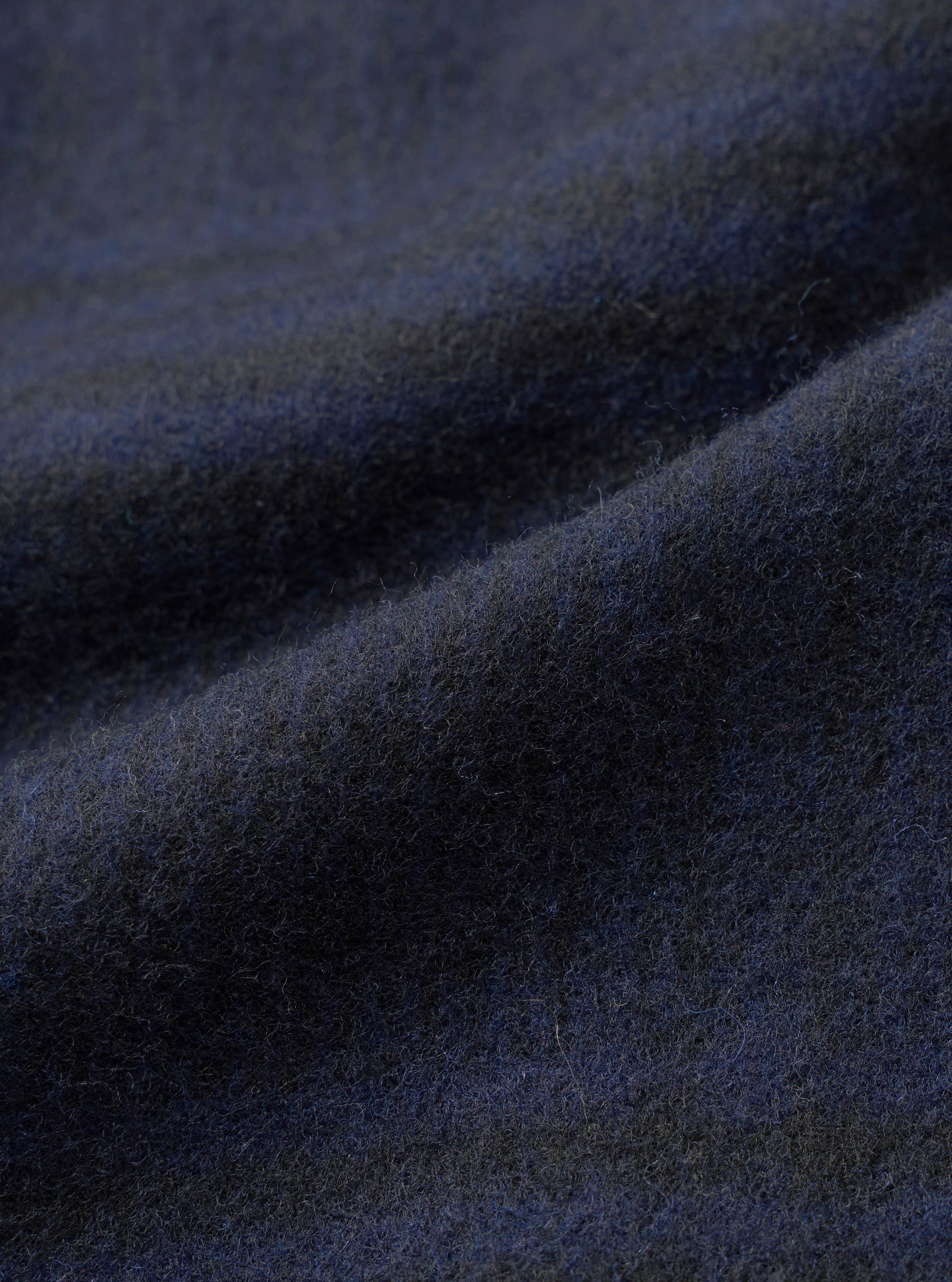Close-up of the navy wool mix fabric used in the Kyoto Work Jacket. The brushed, softly felted surface shows fine individual fibres and a subtle dark mélange tone. Gentle folds across the cloth highlight its weight and texture.