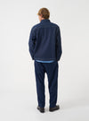 A back view of a model wearing the Indigo Future Denim Troopers Jacket. The image displays the rear construction of the dark blue sustainable denim garment with a straight hem set against a plain neutral backdrop.