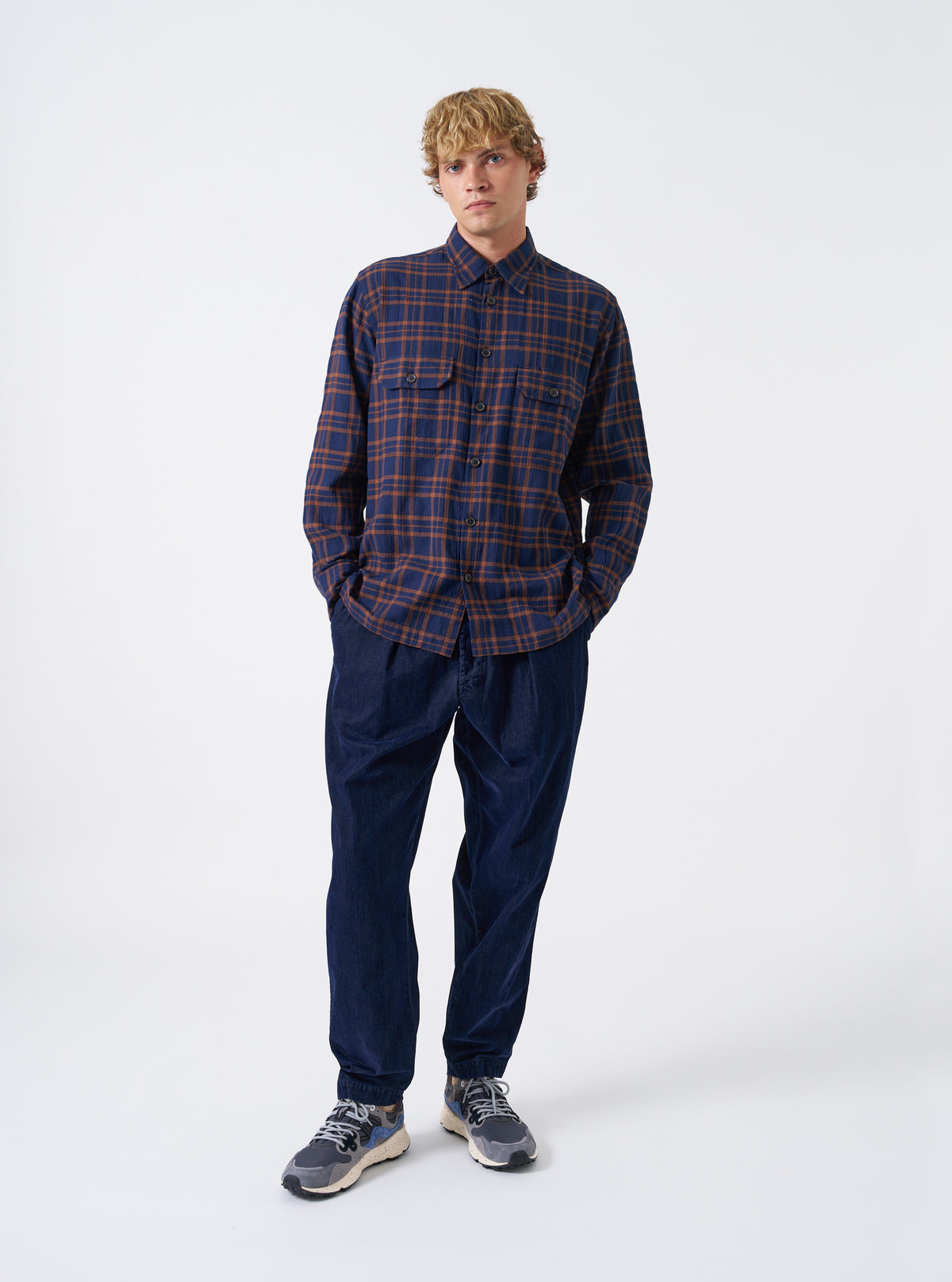 A model wearing the Navy/Brown Young Check CPO Shirt, viewed from the front. The checked shirt features a full button front, chest patch pockets, and a classic pointed collar set against a plain background.