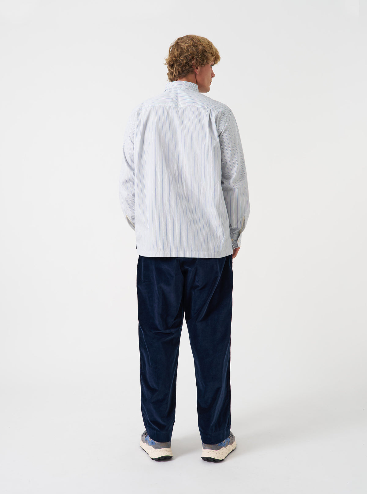 A back view of a model wearing the Grey Stripe Refab Compact Cotton Lucky Shirt. The image highlights the fine grey vertical stripes across the back yoke and relaxed fit set against a plain neutral backdrop.