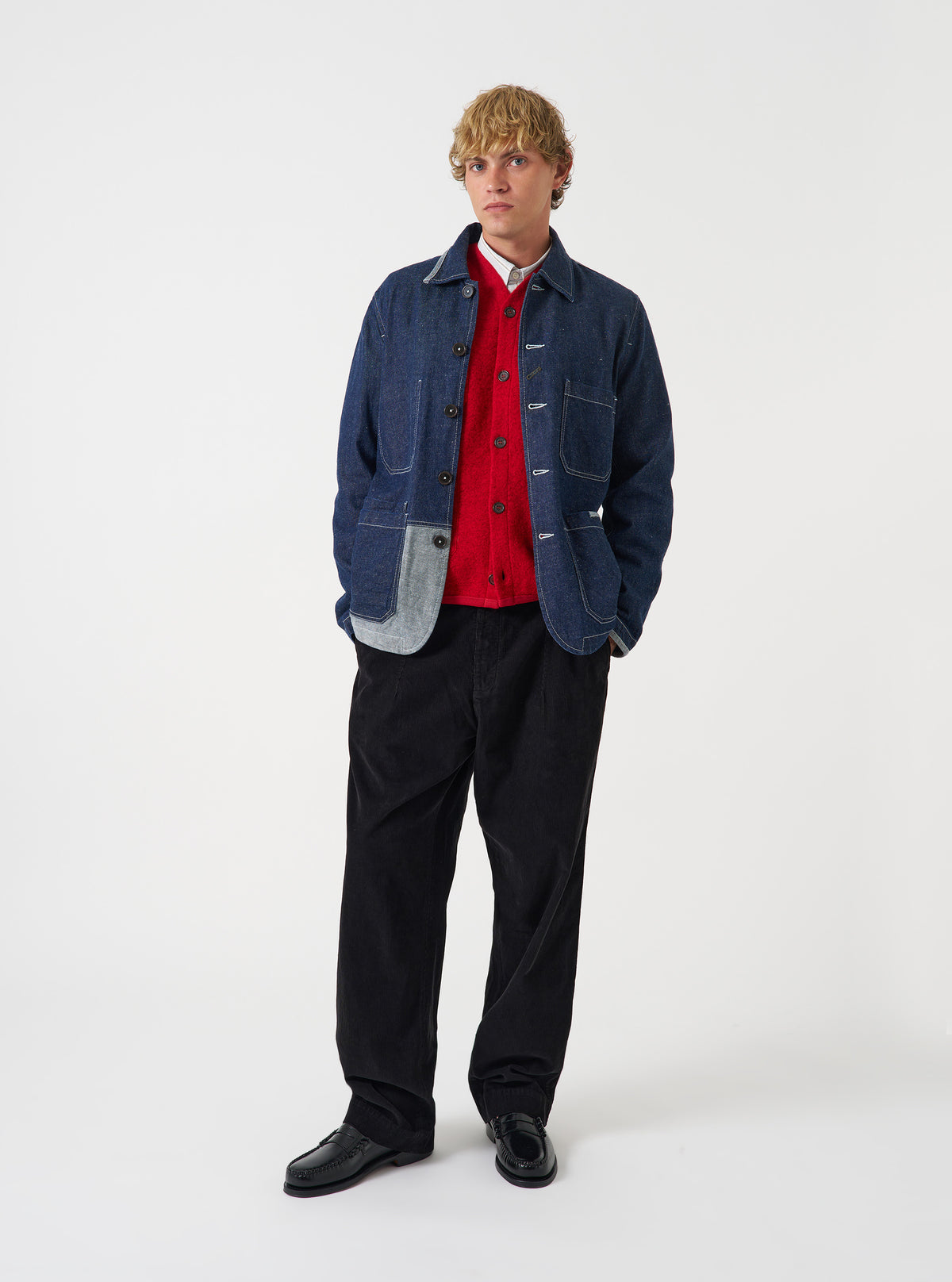 A model wearing the Universal Works Indigo Future Denim OG Bakers Chore Jacket, shown from the front. The dark blue denim jacket features a classic collar, central button fastening, and multiple front patch pockets against a plain background.