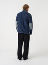 A back view of a model wearing the Universal Works Indigo Future Denim OG Bakers Chore Jacket. The image showcases the rear cut of the deep indigo denim jacket, clean shoulders, and relaxed fit set against a plain backdrop.