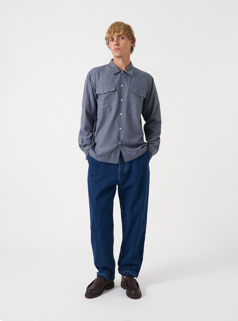A model wearing the Universal Works Blue/Brown Parker Check Attendant Shirt, shown from front. The long-sleeve shirt features a blue and brown check pattern, flat collar, front button fastening, and chest flap pockets against a plain background.