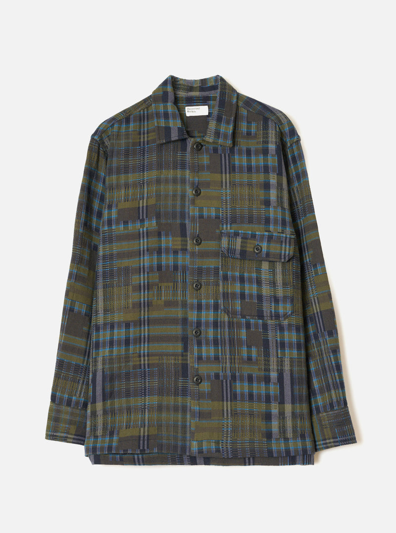 The Olive Shadows Check Fatigue Shirt is laid flat on a light grey backdrop. Shows an olive, navy, and teal plaid patterned weave, open camp collar, five-button front closure, single buttoned flap chest pocket, and long sleeves with plain cuffs.