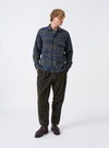 A model wearing the Olive Shadows Check Fatigue Shirt shown from the front. The olive green check overshirt features two front patch chest pockets, a neat collar, and button-down front fastening against a plain backdrop.