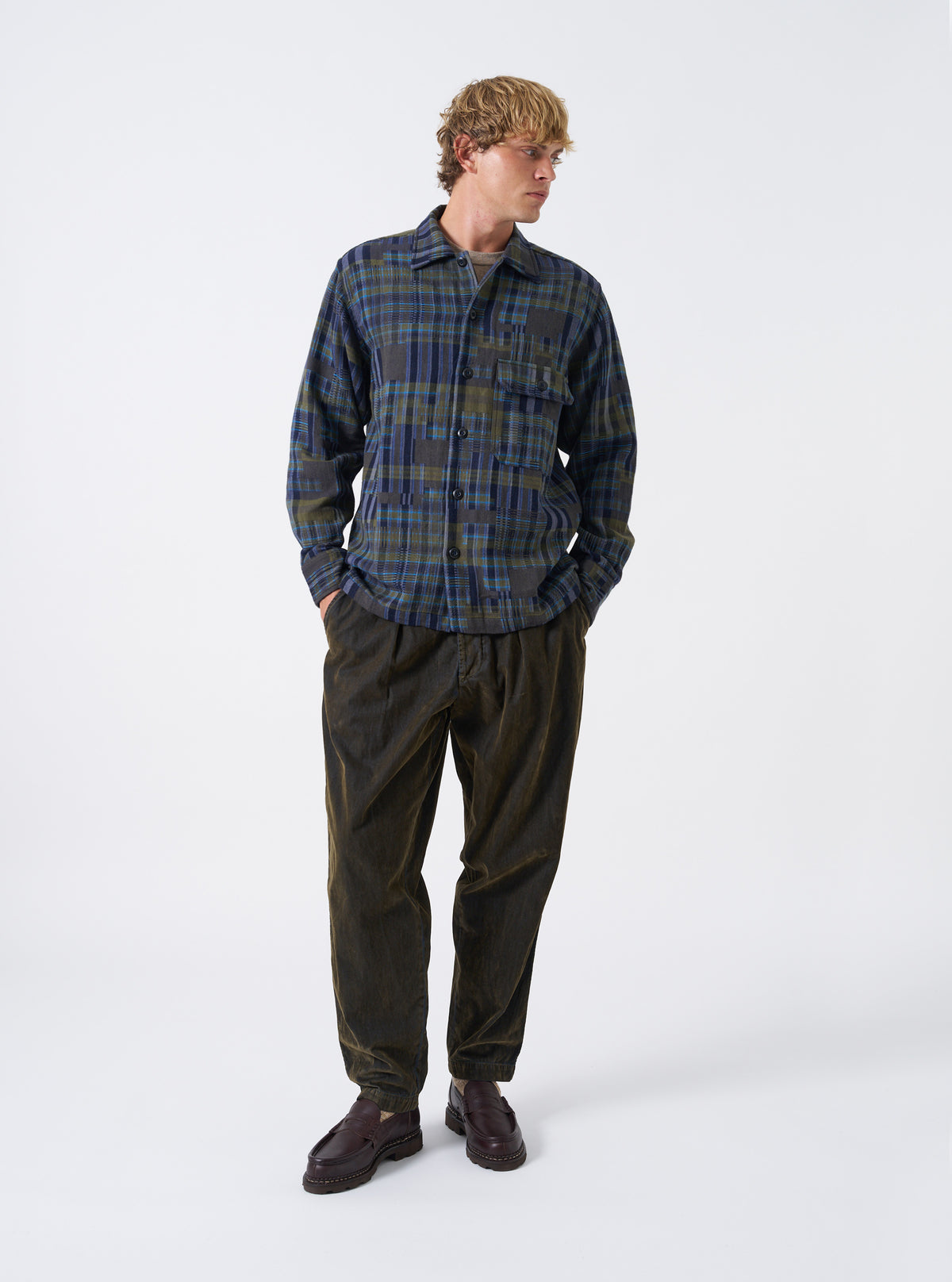 A model wearing the Olive Shadows Check Fatigue Shirt shown from the front. The olive green check overshirt features two front patch chest pockets, a neat collar, and button-down front fastening against a plain backdrop.