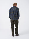 A back view of a model wearing the Olive Shadows Check Fatigue Shirt. The image highlights the relaxed back yoke, olive green check pattern across the cotton fabric, and straight lower hemline against a neutral background.