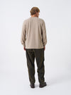 Rear view of a model wearing the Universal Works Olive Flock Chambray Pleated Track Pant standing against a neutral studio background. Showcases the smooth back drape, back pocket positioning, and relaxed silhouette.