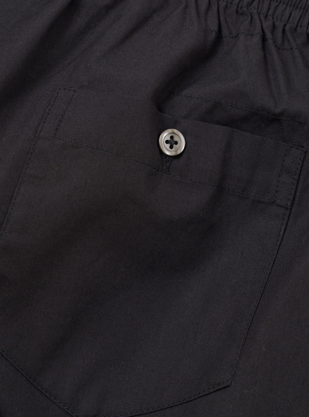 Rear view of the Universal Works Black Broadcloth Boxer Shorts laid flat against a plain backdrop. Showcases the clean back seams, elastic waistband, and smooth texture of the black cotton broadcloth fabric.