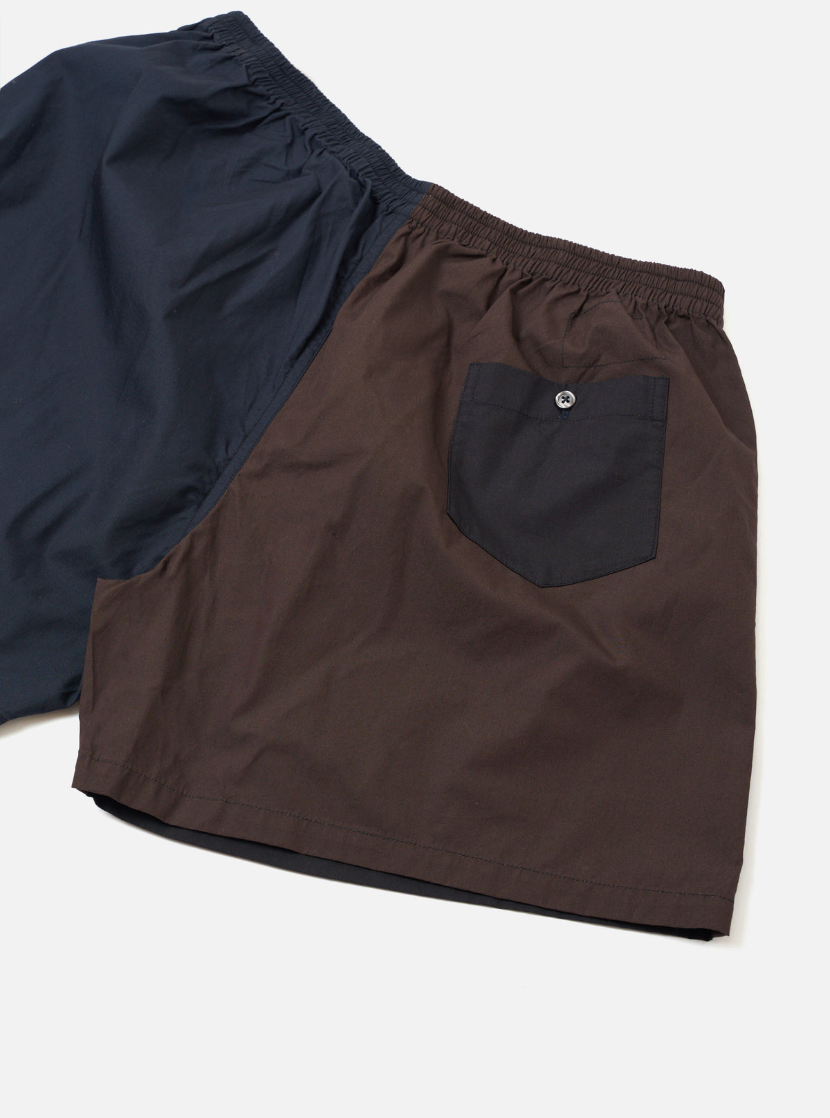 Rear view of the Universal Works Mix Broadcloth Boxer Shorts on a plain studio backdrop. Highlights the back multi-colored patchwork paneling and elastic waistband constructed from cotton broadcloth fabric.