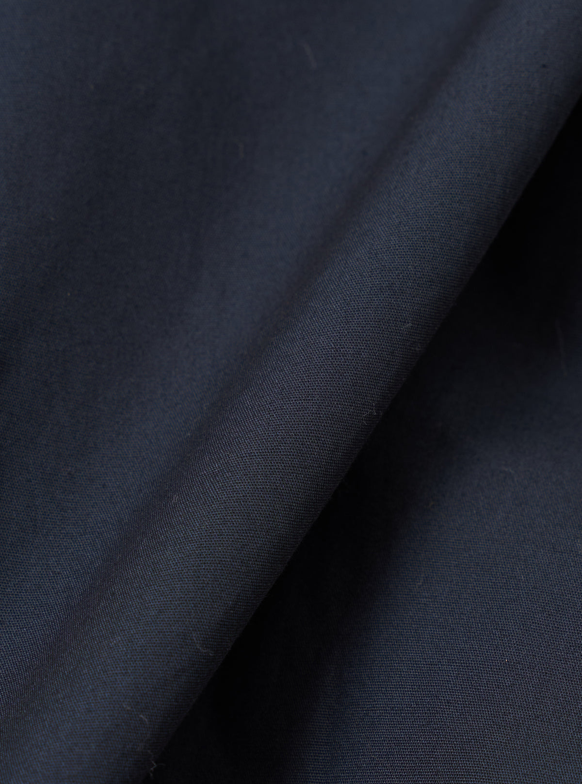 Close-up fabric swatch of the Navy Broadcloth Boxer Shorts by Universal Works. Highlights the tight weave, deep navy shade, and smooth surface of the cotton broadcloth fabric against a plain background.