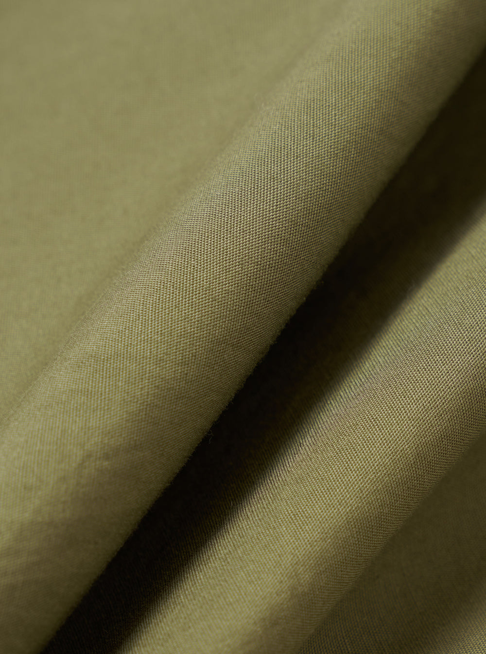 A close-up fabric swatch shot showing the texture and weave of the Universal Works Olive Broadcloth Boxer Shorts fabric, detailing the smooth olive green cotton plain-weave material.