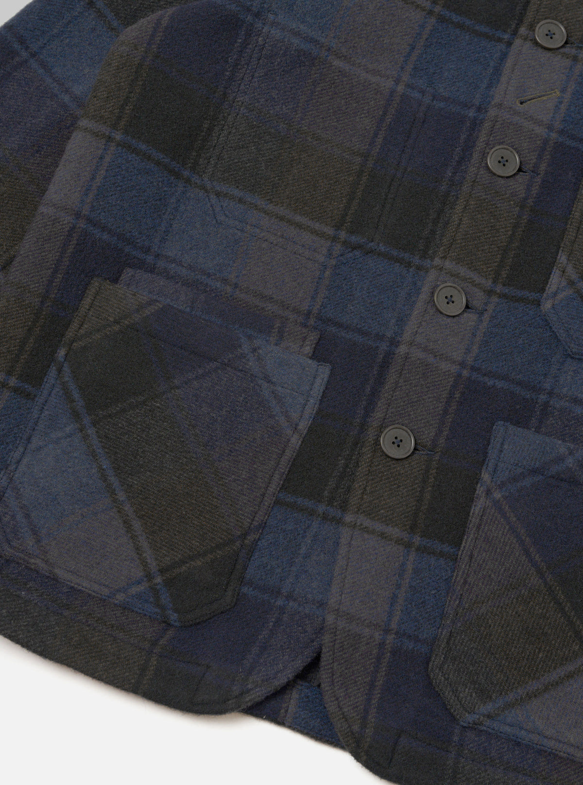 A detailed close-up shot of the Universal Works Navy/Brown Berlin Wool Check OG Bakers Chore Jacket on a plain background, highlighting the signature angled top buttonhole and classic collar details.