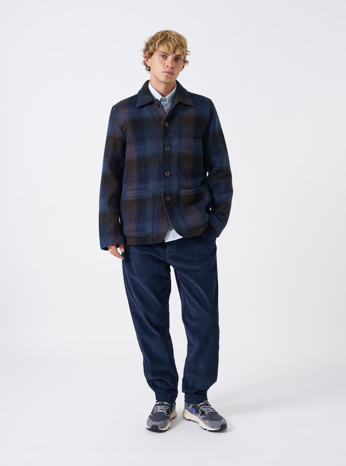 A model wearing the Universal Works Navy/Brown Berlin Wool Check OG Bakers Chore Jacket, viewed from the front against a plain background. The model showcases the loose fit and front pocket styling of the jacket.