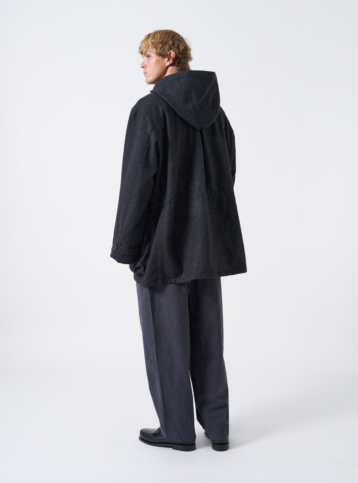 A back view of a model wearing the Universal Works Grey Marl Mowbray Boston Parka against a plain background, displaying the relaxed fit, generous hood coverage, and textured grey marl fabric construction.