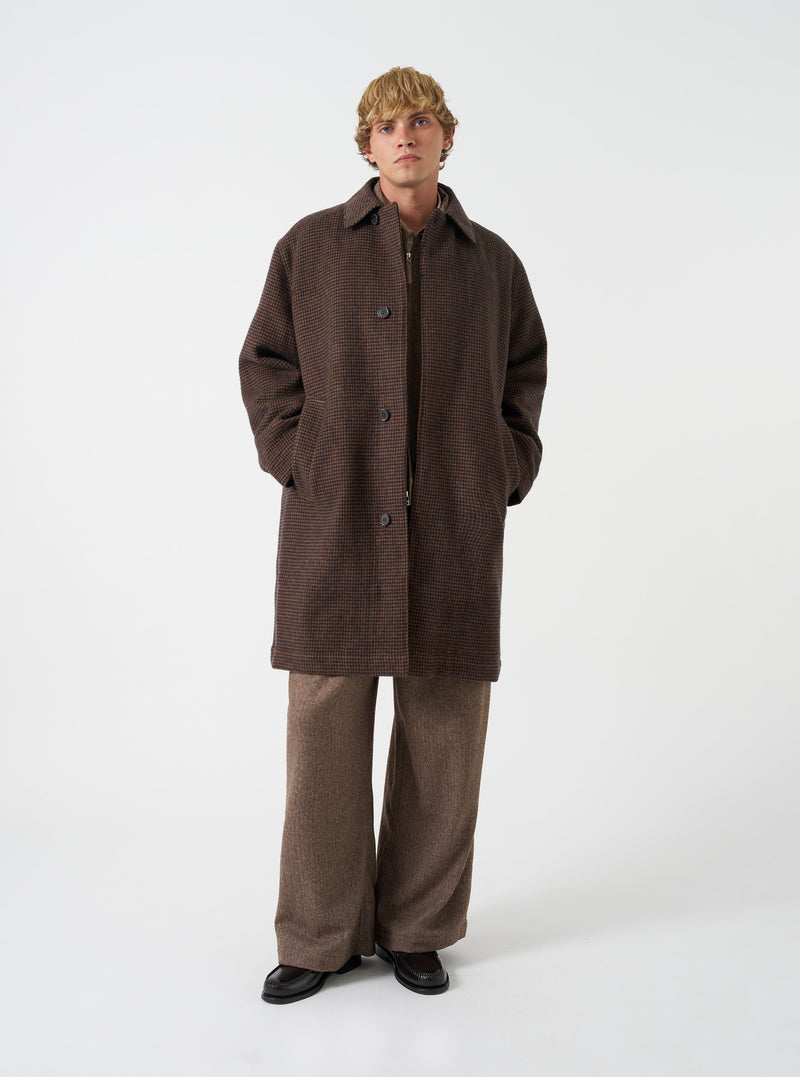 A model wearing the Navy/Brown Wool Tweed Mix Stan Coat, captured from the front against a plain background. The long overcoat is worn unbuttoned over layering pieces, showing its relaxed silhouette, lapels, and wool tweed texture.