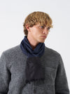 A model wearing the Universal Works Black/Blue Jacquard Silk Scarf wrapped around the neck. The lightweight silk accessory features a woven black and blue pattern, smooth finish, and elegant drape set against a plain neutral background.