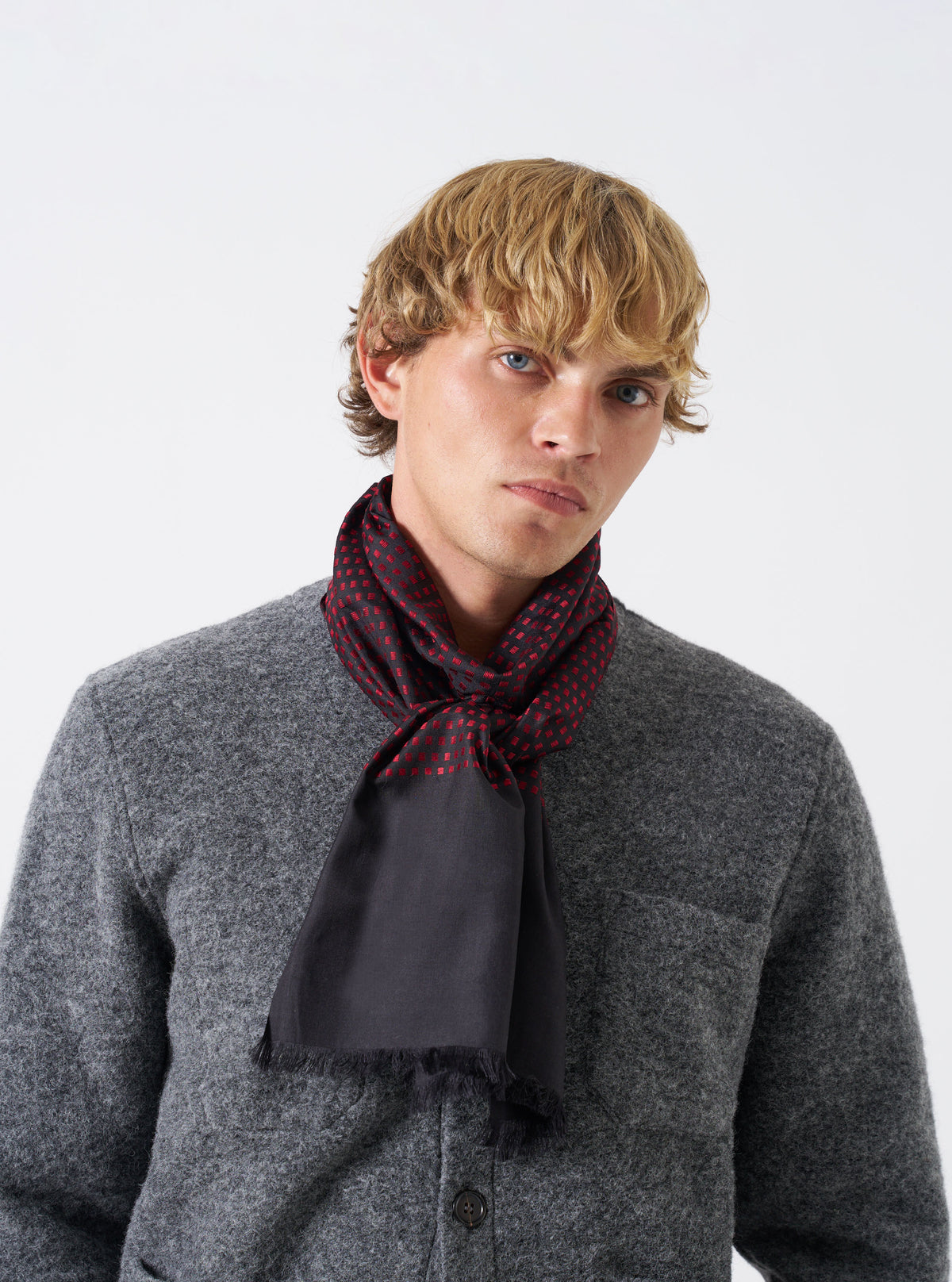 A model wearing the Universal Works Black/Red Jacquard Silk Scarf draped neatly around the neck. The silk scarf displays a woven black and red pattern with a soft texture, accentuating the outfit against a plain light backdrop.