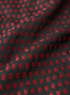 A detailed swatch shot of the Universal Works Black/Red Jacquard Silk Scarf fabric. The close-up shot highlights the fine silk weave and rich contrast of black and red yarns set against a plain backdrop.