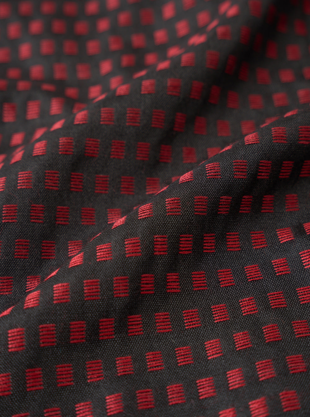 A detailed swatch shot of the Universal Works Black/Red Jacquard Silk Scarf fabric. The close-up shot highlights the fine silk weave and rich contrast of black and red yarns set against a plain backdrop.