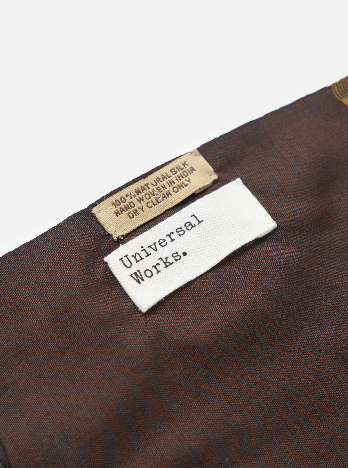 A draped view of the Universal Works Brown/Sky/Gold Jacquard Silk Scarf, displaying its soft handle and light fold lines. The multi-coloured silk scarf is featured prominently against a plain background.