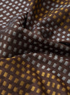 A close-up macro image of the Universal Works Brown/Sky/Gold Jacquard Silk Scarf fabric swatch. The detailed image showcases the texture of the pure silk jacquard weave and its distinct colour pattern.