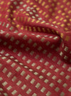 A detailed close-up swatch shot of the Universal Works Red/Silver/Gold Jacquard Silk Scarf. The macro view emphasizes the fine weave of red silk intertwined with silver and gold threads against a plain backdrop.