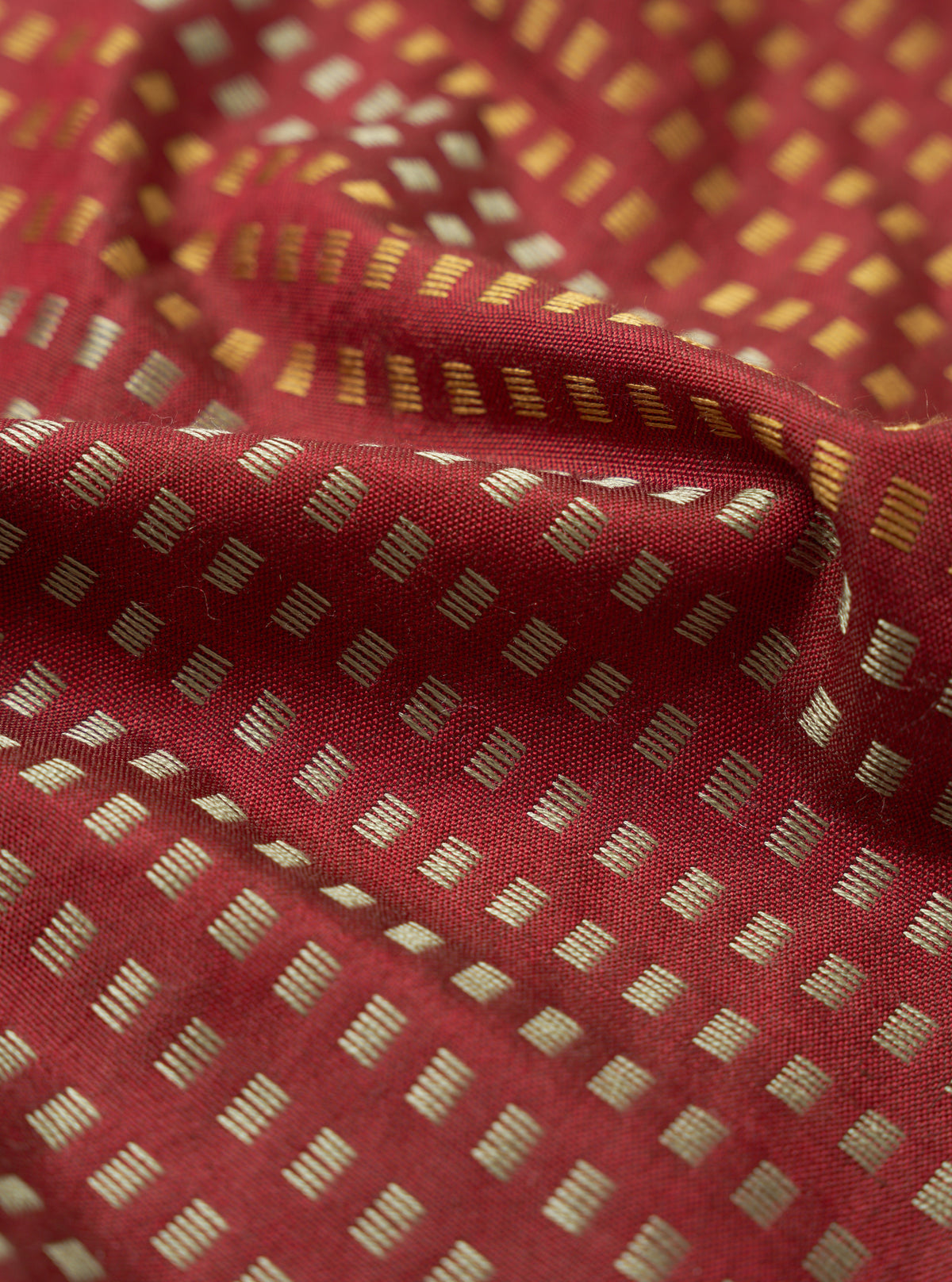 A detailed close-up swatch shot of the Universal Works Red/Silver/Gold Jacquard Silk Scarf. The macro view emphasizes the fine weave of red silk intertwined with silver and gold threads against a plain backdrop.