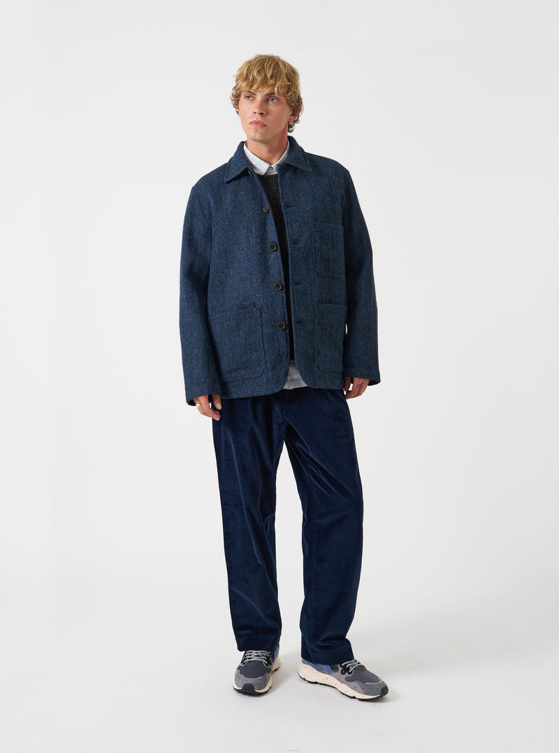 A model wearing the Blue/Black Harris Tweed OG Bakers Chore Jacket, photographed from the front against a plain background. The chore jacket is styled open over a top, showing its collar and front patch pockets.