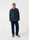 A model wearing the Blue/Black Harris Tweed OG Bakers Chore Jacket, photographed from the front against a plain background. The chore jacket is styled open over a top, showing its collar and front patch pockets.