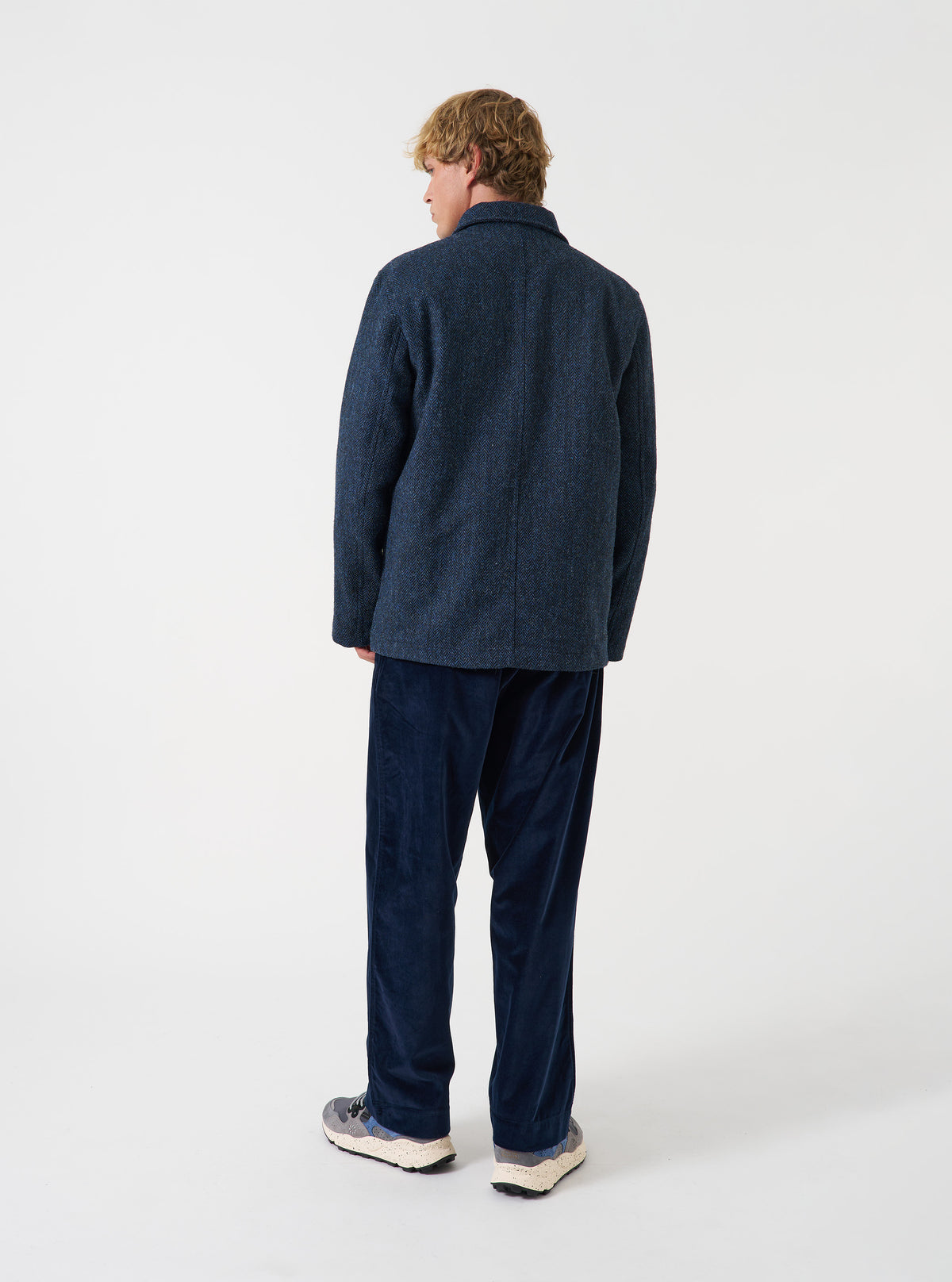 A model wearing the Blue/Black Harris Tweed OG Bakers Chore Jacket, viewed from behind against a plain background. The image displays the relaxed fit, straight hem, and back panel of the dark tweed jacket.