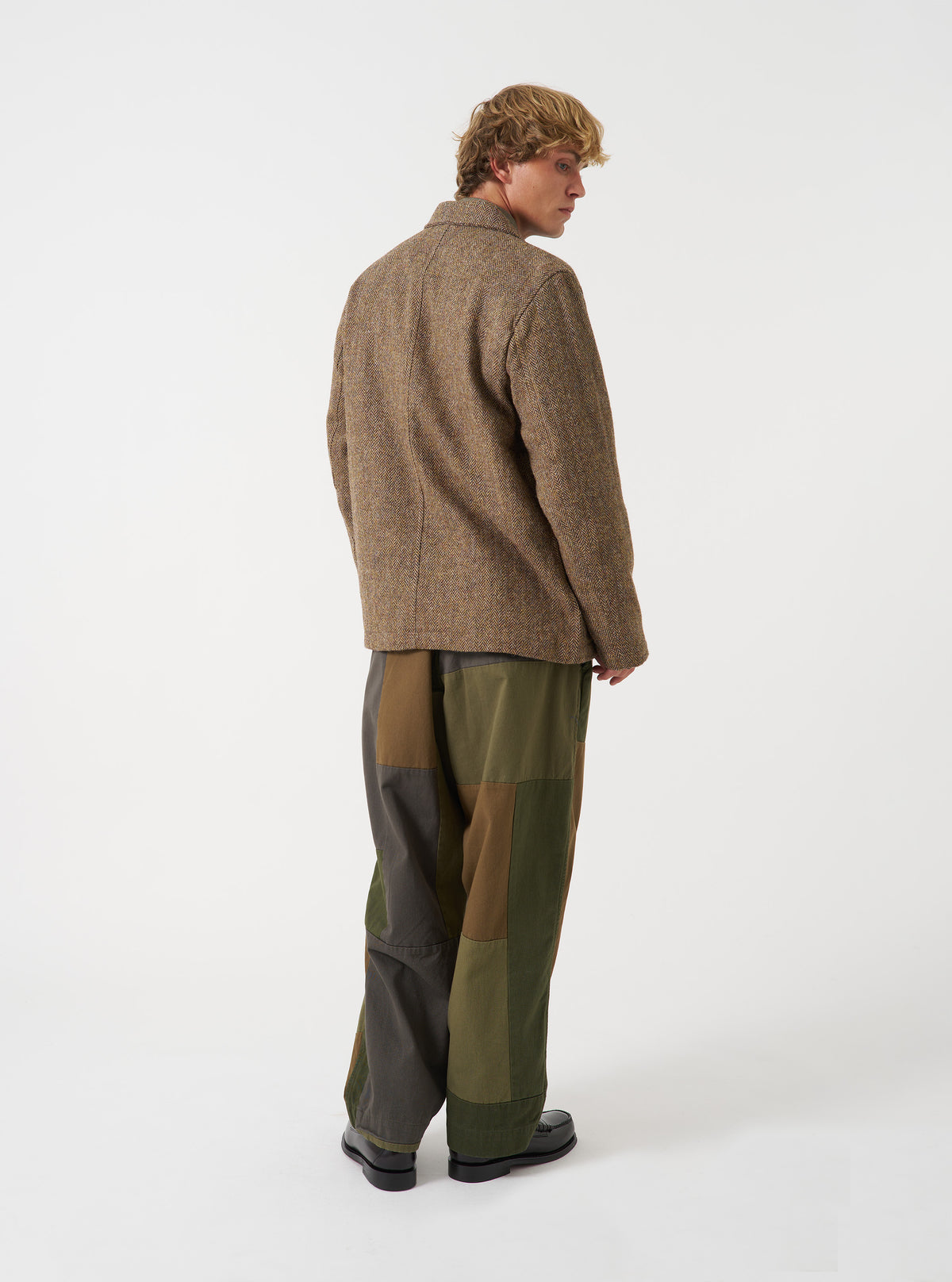 A model wearing the Sand/Brown Harris Tweed OG Bakers Chore Jacket, viewed from the rear. The image displays the back panel of the patterned wool jacket and structured shoulder seam set against a plain neutral background.
