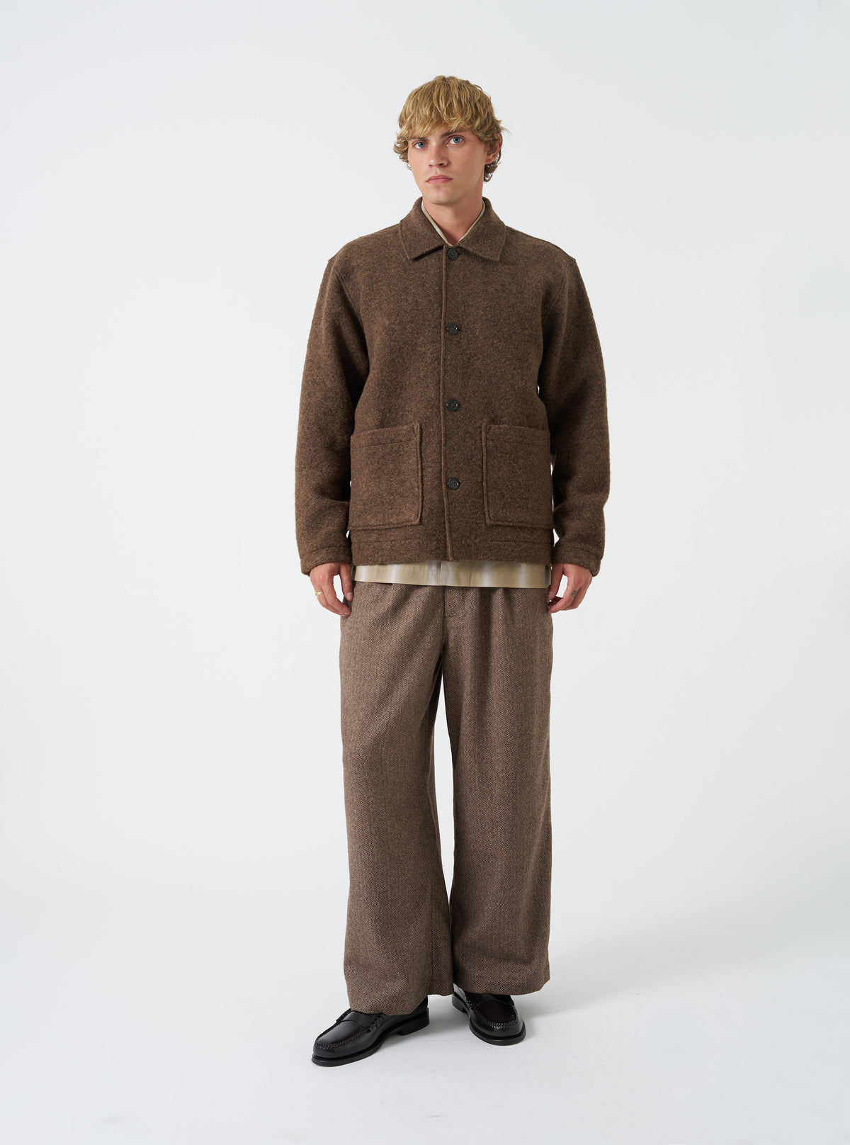 A model wearing the Brown Wool Herringbone Gillespie Pant, shown from the front against a plain backdrop. The trousers feature a brown herringbone wool pattern, tailored legs, and side slant pockets.